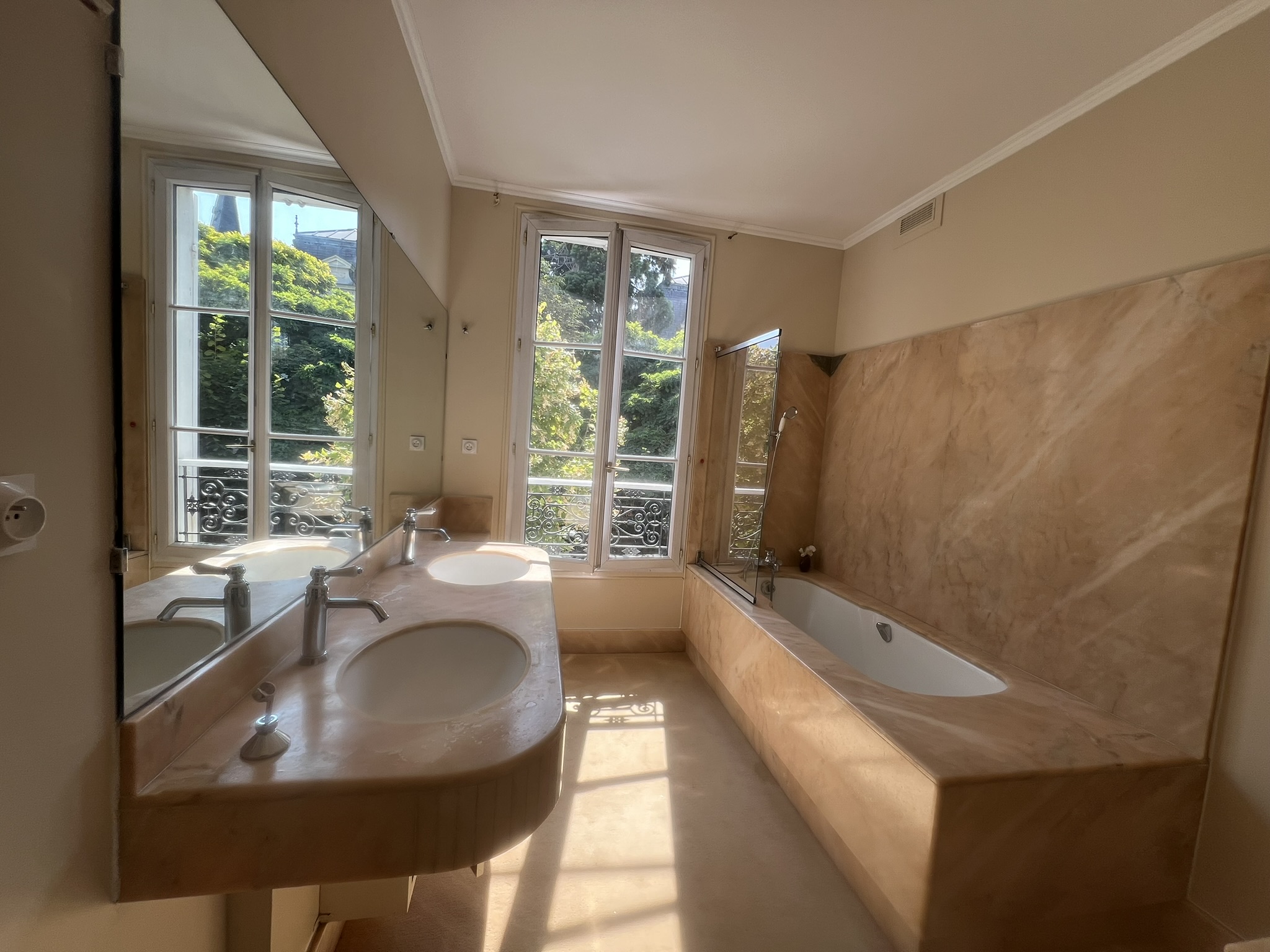 Salle de bain rénovée d’une maison de style château à Enghien-les-Bains – murs peints en ton beige doux, revêtements effet marbre, double vasque et baignoire lumineuse